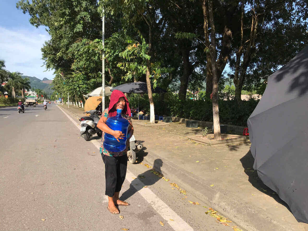 Giữa thời tiết gần 40 độ C, cô Hạnh vẫn gò lưng ôm bình nước lớn, tất tả mưu sinh trên vỉa hè. Ảnh: Yên San